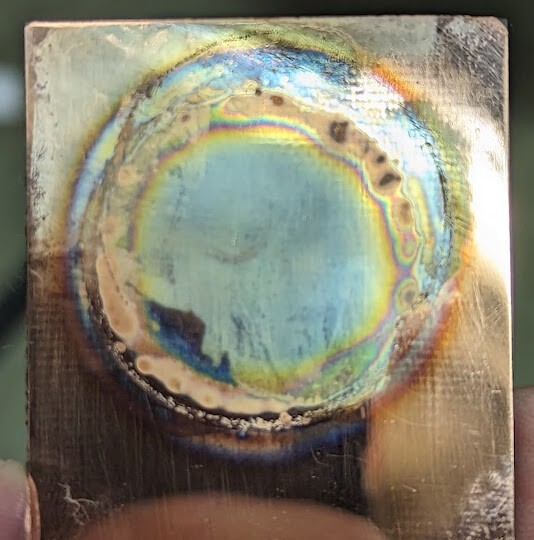 A bit of copper board with a messy coloured circle of silver and other stuff on it. 
It's my attempt at a becquerel daguerreotype in a lunchtime. 